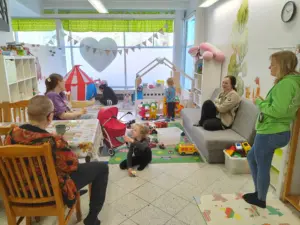 Lapsiperheiden kohtaamispaikan Lähiötalon leikkitilassa lapset leikkimässä lattialla ja vanhemmat keskustelevat keskenään. Taustalla näkyy mm. sohva, leikkitelta ja paljon värikkäitä leluja.